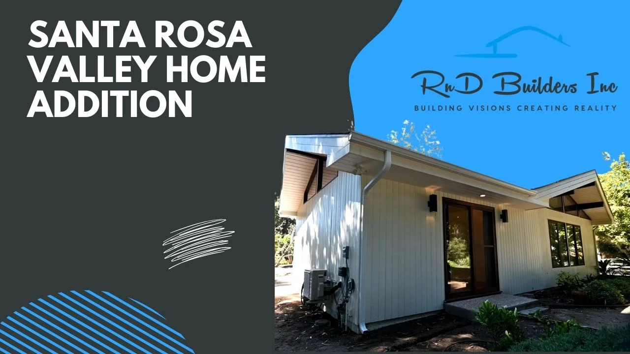 Exterior home addition with white vertical board siding, low-pitch roof, and dark-framed sliding glass door by RnD Builders Inc